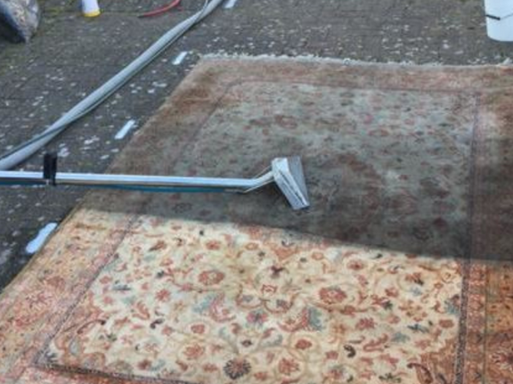 This is a photo of a floral rug that is being steam cleaned. The bottom half has been completed and the top half is being done works carried out by Abbots Langley Carpet Cleaning