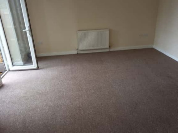 This is a photo of a living room after it has been cleaned. The room is empty and has a brown carpet that has been steam cleaned works carried out by Abbots Langley Carpet Cleaning